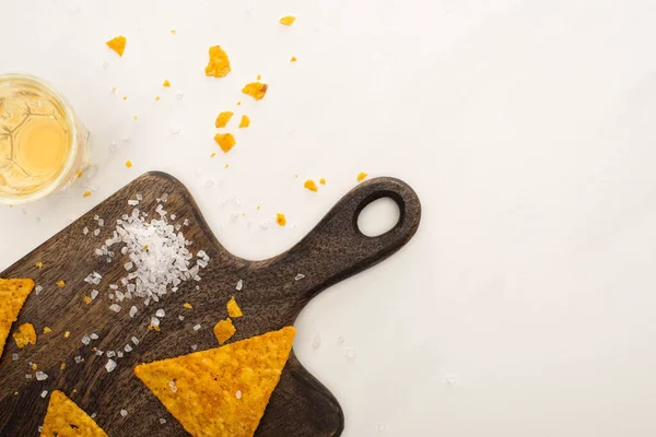Top view of golden tequila with salt and nachos on wooden cutting board on white marble surface — Stock Photo
