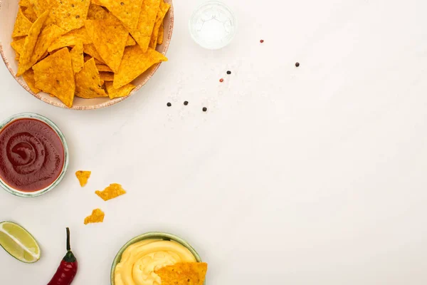 Top view of tequila with lime, chili pepper, sauces and nachos on white marble surface — Stock Photo