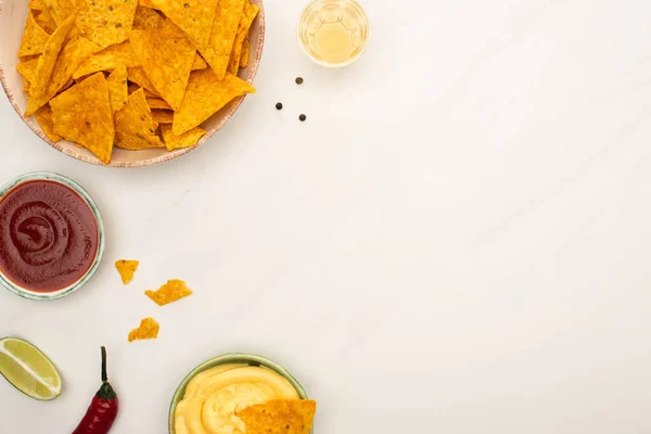 Top view of tequila with lime, chili pepper, sauces and nachos on white marble surface — Stock Photo