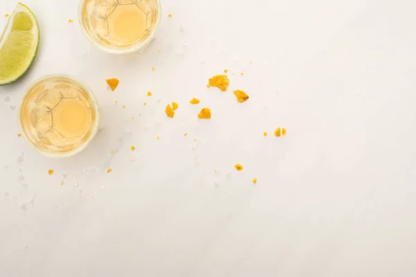 Top view of golden tequila in shot glasses with lime and nachos crumbs on white marble surface — Stock Photo
