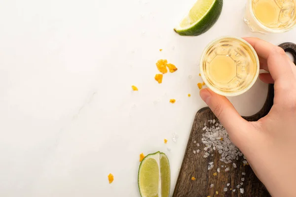 Abgeschnittene Ansicht einer Frau, die goldenen Tequila mit Limette trinkt, Salz auf weißem Marmor — Stockfoto