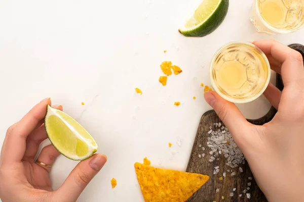 Vista cortada de mulher bebendo tequila dourada com limão, sal na superfície de mármore branco — Fotografia de Stock