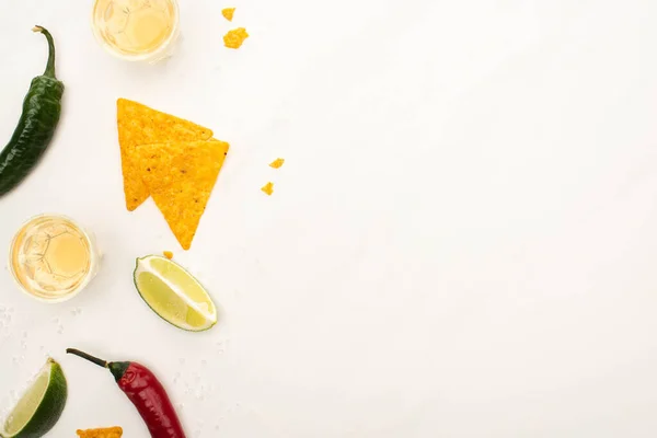 Top view of golden tequila with lime, chili peppers, nachos on white marble surface — Stock Photo