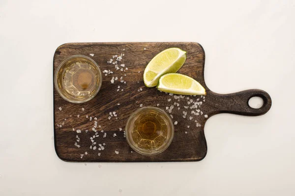 Blick von oben auf goldenen Tequila mit Kalk, Salz auf Holzschneidebrett auf weißem Marmor — Stockfoto