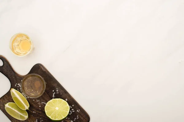 Вид зверху на золоту текілу з лаймом, сіль на дерев'яній обробній дошці на поверхні білого мармуру — стокове фото