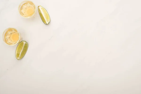 Vista dall'alto di tequila dorata con calce su superficie di marmo bianco — Foto stock