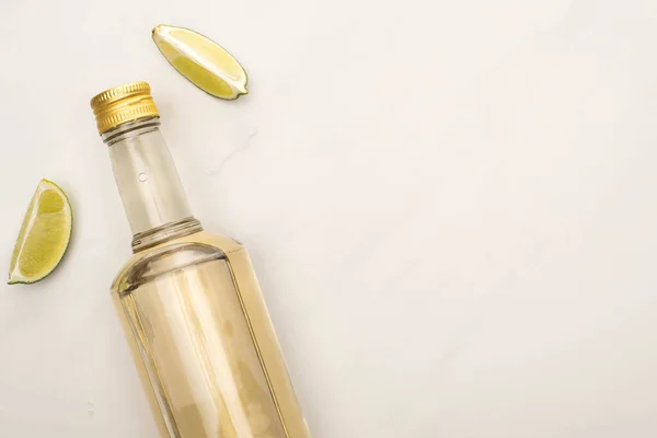 Vue du dessus de la tequila dorée en bouteille avec de la chaux sur la surface de marbre blanc — Photo de stock
