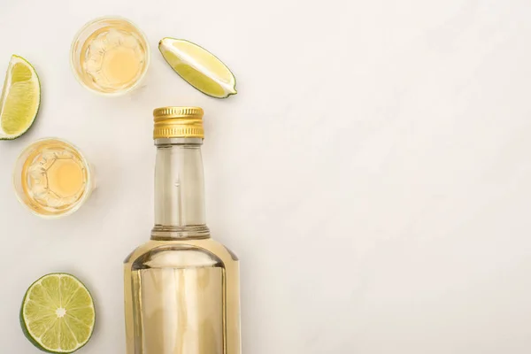 Top view of golden tequila in bottle and shot glasses with lime on white marble surface — Stock Photo