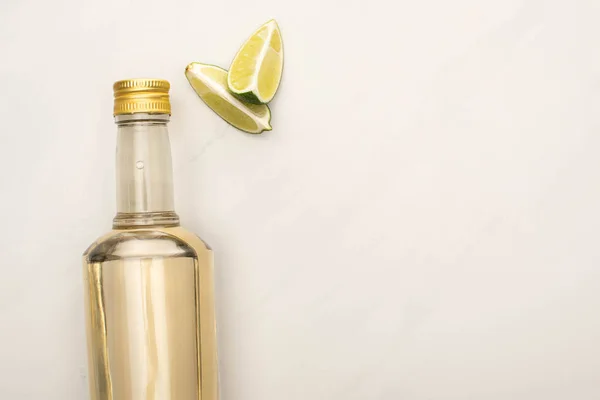 Vue du dessus de la tequila dorée en bouteille avec de la chaux sur la surface de marbre blanc — Photo de stock