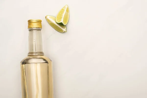 Draufsicht auf goldenen Tequila in Flasche mit Limette auf weißem Marmor — Stockfoto