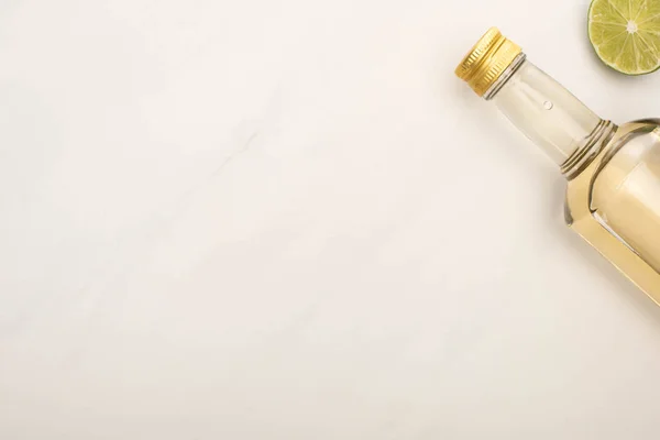 Вид сверху на золотую текилу в бутылке с лаймом на поверхности белого мрамора — стоковое фото