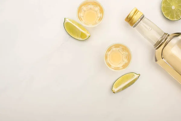 Top view of golden tequila in bottle and shot glasses with lime on white marble surface — Stock Photo