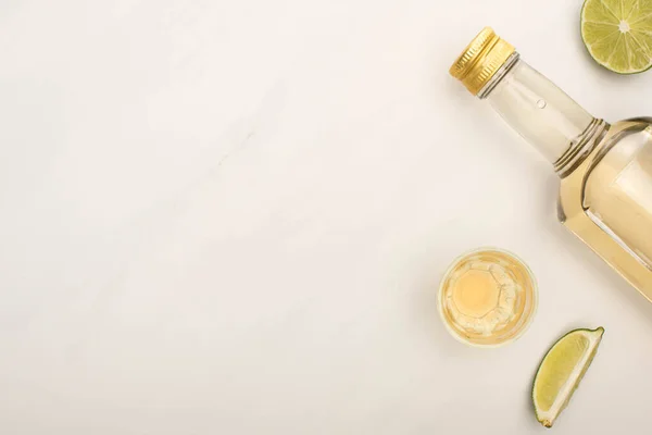 Vue de dessus de la tequila dorée en bouteille et verre de tir avec de la chaux sur la surface de marbre blanc — Photo de stock