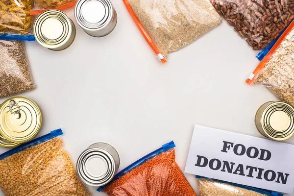 Vista superior de latas e grumos em sacos de zíper perto do cartão com letras de doação de alimentos no fundo branco — Fotografia de Stock