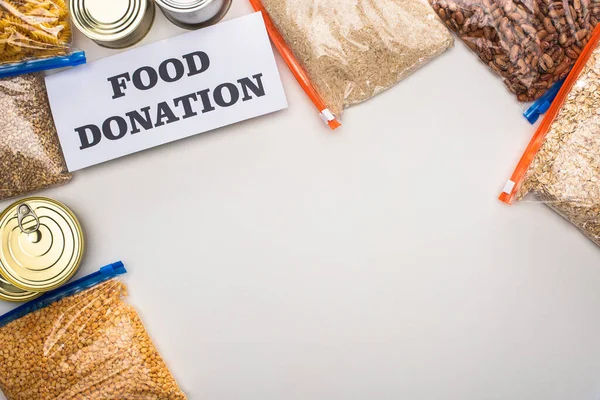 Top view of cans and groats in zipper bags near card with food donation lettering on white background — Stock Photo