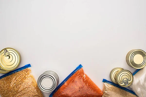 Draufsicht auf Dosen und Grütze in Reißverschlusstaschen auf weißem Hintergrund, Konzept der Lebensmittelspende — Stockfoto