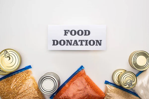 Top view of cans and groats in zipper bags near card with food donation lettering on white background — Stock Photo