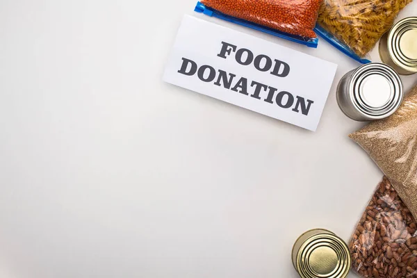 Top view of cans and groats in zipper bags near card with food donation lettering on white background — Stock Photo