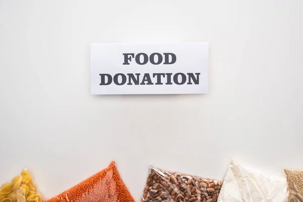 Vista superior de massas e grumos em sacos de zíper perto do cartão com letras de doação de alimentos no fundo branco — Fotografia de Stock