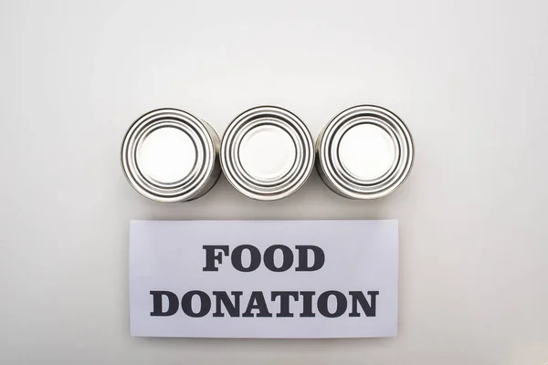 Flat lay with cans on white background with food donation card — Stock Photo