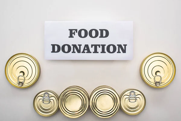 Vista superior de latas con comida enlatada sobre fondo blanco con tarjeta de donación de alimentos - foto de stock