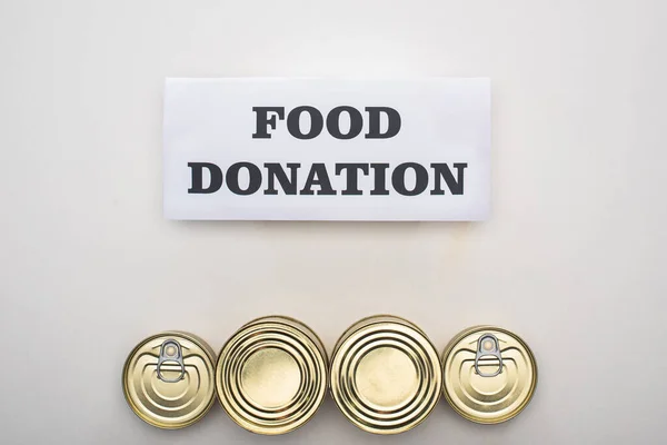 Vista superior de latas con comida enlatada sobre fondo blanco con tarjeta de donación de alimentos - foto de stock