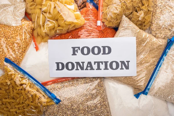 Top view of groats and pasta in zipper bags and card with food donation lettering — Stock Photo