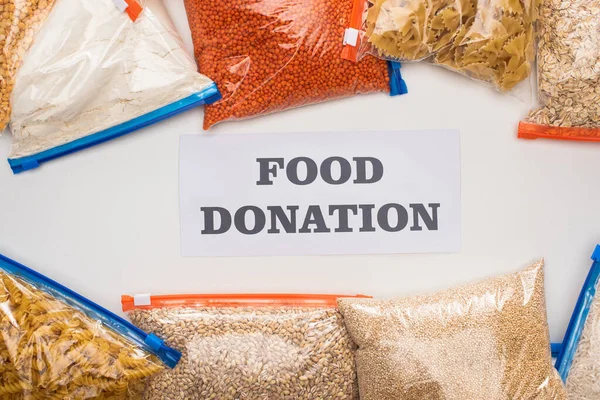 Top view of groats and pasta in zipper bags near card with food donation lettering on white background — Stock Photo