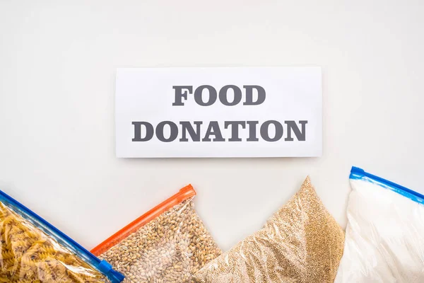 Top view of groats and pasta in zipper bags near card with food donation lettering on white background — Stock Photo