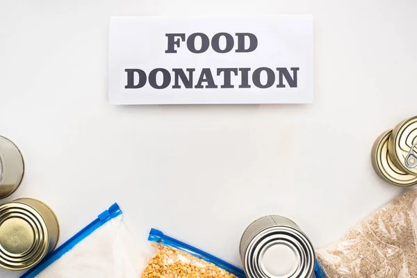 Top view of cans and groats in zipper bags near card with food donation lettering on white background — Stock Photo