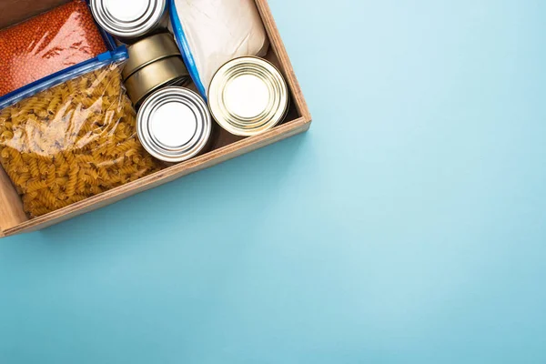 Vista superior de latas y grañones en bolsas con cremallera en caja de madera sobre fondo azul - foto de stock