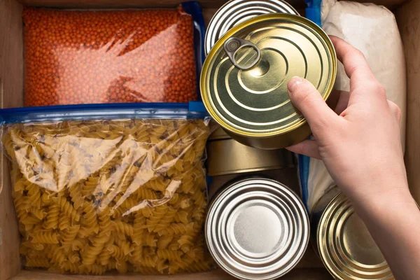 Vista ritagliata di donna che tiene stagno sopra i cereali in sacchetti con cerniera, concetto di donazione di cibo — Foto stock