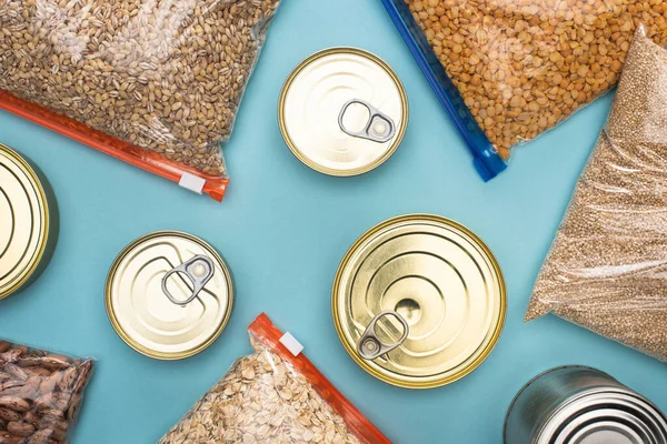 Vista superior de latas e grumos em sacos de zíper no fundo azul, conceito de doação de alimentos — Fotografia de Stock