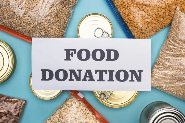 Top view of cans and groats in zipper bags near card with food donation lettering on blue background — Stock Photo