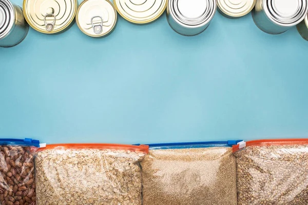 Draufsicht auf Dosen und Grütze in Reißverschlusstaschen auf blauem Hintergrund mit Kopierraum — Stockfoto