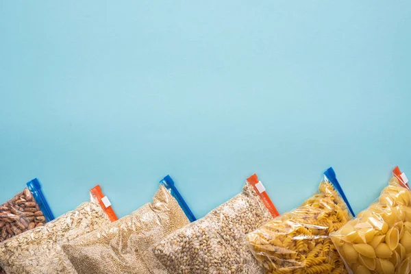 Draufsicht auf Pasta, Bohnen und Grütze in Reißverschlusstaschen auf blauem Hintergrund, Konzept der Lebensmittelspende — Stockfoto