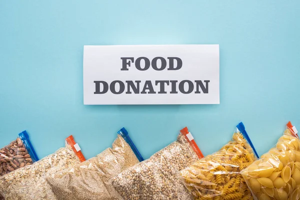 Top view of pasta, beans and groats in zipper bags on blue background with food donation card — Stock Photo