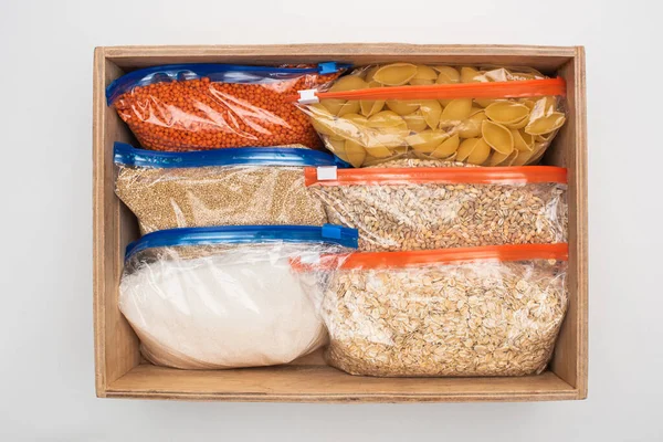 Vista superior de pasta y grañones en bolsas con cremallera en caja de madera sobre fondo blanco, concepto de donación de alimentos - foto de stock