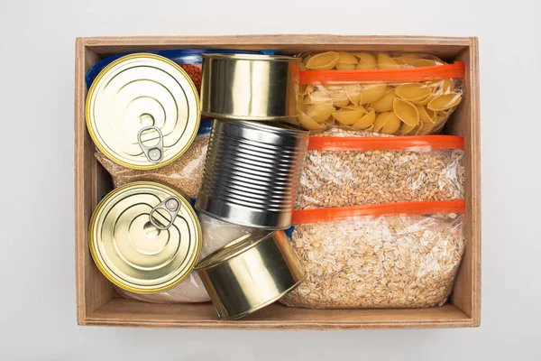 Vista superior de latas e grumos em sacos de zíper em caixa de madeira no fundo branco, conceito de doação de alimentos — Fotografia de Stock