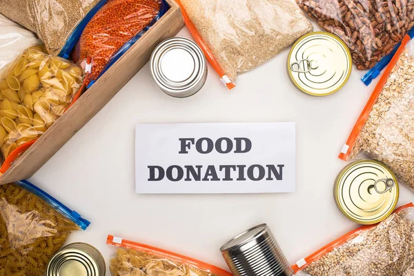 Top view of cans and groats in zipper bags in wooden box on white background with food donation card — Stock Photo