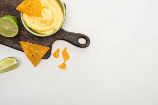Vista dall'alto di nachos di mais con lime, salsa di formaggio su tagliere di legno su sfondo bianco — Foto stock