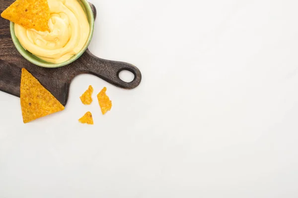 Vista dall'alto di nachos di mais con salsa di formaggio su tagliere di legno su sfondo bianco — Foto stock