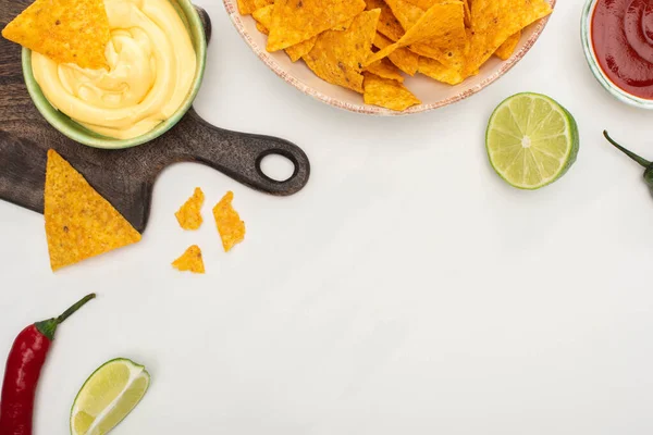 Vista superior de nachos de milho com pimenta, limão, ketchup, molho de queijo em tábua de corte de madeira no fundo branco — Fotografia de Stock