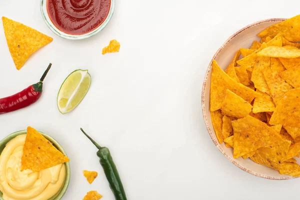 Top view of corn nachos with lime, chili peppers, ketchup and cheese sauce on white background — Stock Photo