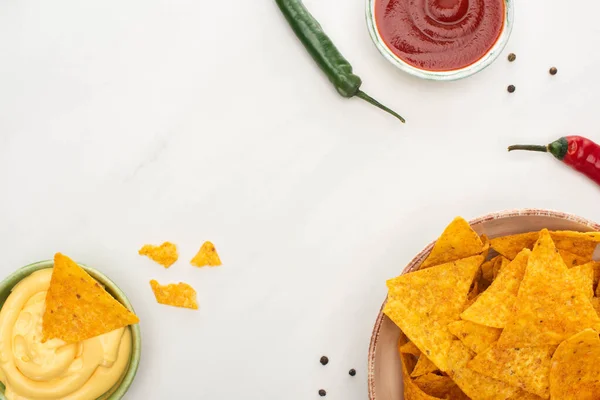 Top view of corn nachos with chili peppers, ketchup and cheese sauce on white background — Stock Photo