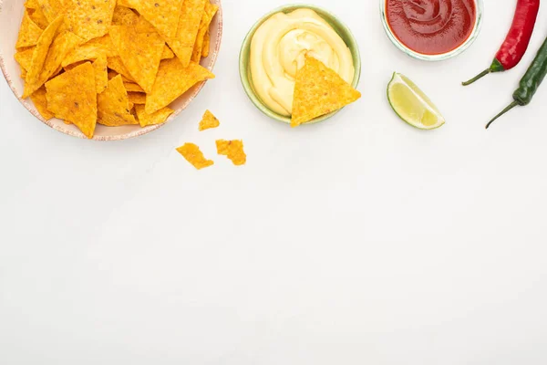 Vista superior de nachos de maíz con lima, chiles, salsa de ketchup y queso sobre fondo blanco - foto de stock