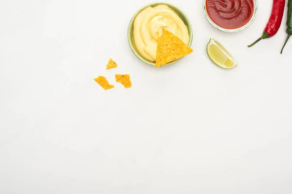 Vue du dessus des nachos de maïs avec citron vert, piments, ketchup et sauce au fromage sur fond blanc — Photo de stock