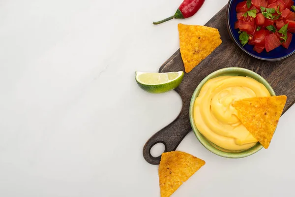 Top view of corn nachos with lime, chili and cheese sauce on wooden cutting board on white background — Stock Photo