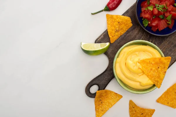 Top view of corn nachos with lime, chili and cheese sauce on wooden cutting board on white background — Stock Photo