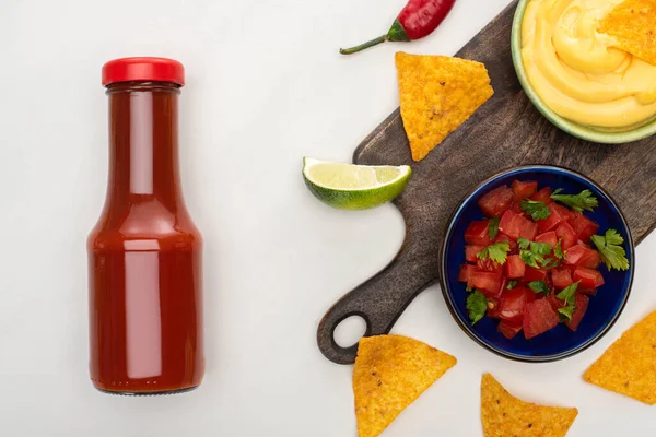 Vista superior de nachos de milho com limão, pimenta, ketchup e molho de queijo em tábua de corte de madeira sobre fundo branco — Fotografia de Stock